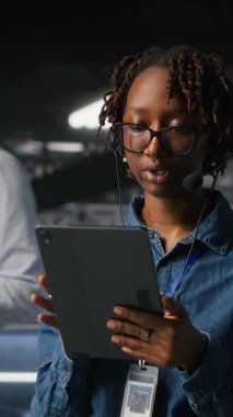 Dikey Veri Merkezi çalışanı mikrofonla konuşurken aşağıdaki yapay zeka platformlarının bakımını denetliyor. IT uzmanı makine öğrenme sistemini koordine etmek için tablet kullanır