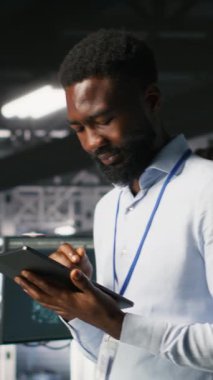 Veri merkezi endüstriyel platformunda dikey video yönetimi tabletteki altyapı performans çıktılarını analiz ediyor. Sunucu odası çalışanı iş görevleri yapıyor, ana bilgisayarları inceliyor, yapılandırmalar, kamera B