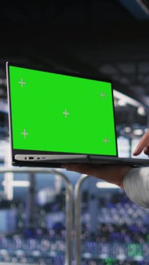 AI LLM görselleştirmesini inceleyen meslektaşının yanındaki yeşil ekran laptop kullanan sunucu çalışanının dikey videosunu kapat. Yapay zeka sistemlerini ve kamerayı izlemek için veri merkezi IT profesyonel kroma anahtar defteri
