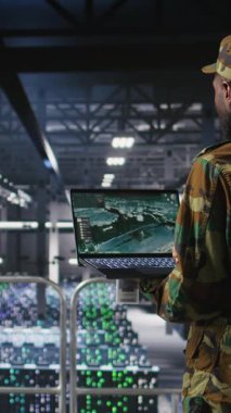 Dikey video teknisyeni, güvenli sunucu merkezindeki laptop ekranında taktik gösterge panelini inceliyor. Not defterinde stratejik iletişim ve altyapı denetim yazılımı kullanan ordu uzmanı