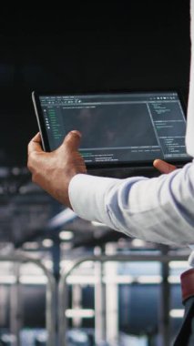 Bulanık arkaplandaki yapay zeka görsellemelerini gözden geçiren meslektaşımın yanındaki tablet üzerindeki dikey video veri merkezi kontrol kodu. Bilişim uzmanları sinirsel ağ çıktılarını analiz etmek ve istikrarlı hale getirmek için aygıt kullanırlar