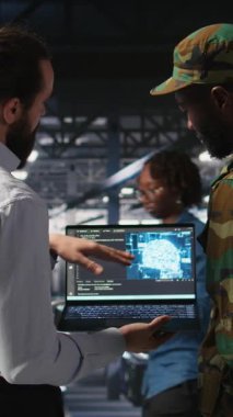 Güvenli veri merkezindeki dikey video teknisyenleri yapay zeka sistemlerini izlemek için dizüstü bilgisayar kullanıyorlar. Ordu operatörleri sunucu merkezinde makine öğrenimi için istikrarlı altyapı sağlıyorlar