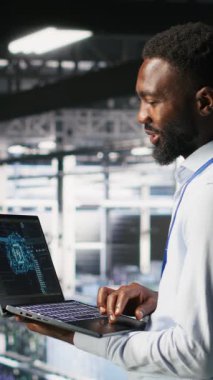 Veri merkezindeki dikey video programcısı ve meslektaşı dizüstü bilgisayardaki AI LLM görselleştirmelerini inceliyor. IT ekip çalışanları, istikrarlı bir altyapı sağlamak için nöral ağ performans çıktılarını analiz ediyor