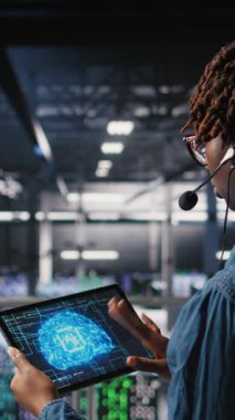 Endüstriyel platformdaki dikey video veri merkezi çalışanı aşağıdaki yapay zeka platformlarının bakımını denetlerken kulaklık mikrofonuyla konuşuyor. Yönetici, derin öğrenme sistemi görevlerini koordine etmek için tablet kullanır