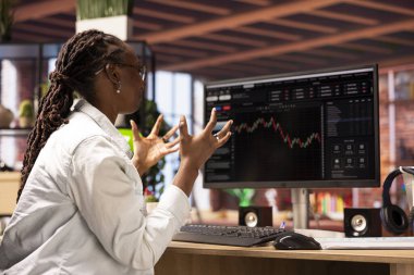 Hüsrana uğramış borsacı üzgün, bilgisayar ekranına bakıyor, düşen hisse senedi fiyatlarını, kırmızı çizelgeleri ve kayıpları gösteriyor. Yatırımcı, monitördeki borsa hisselerinde düşüşe bakarken bunaldı