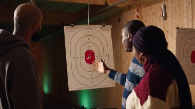 Galeri güvenlik görevlisini vurmak tam puan sistemini ve okuma kurallarını açıklıyor. Atış menzili uzmanı hedef kitle sistemini öğretiyor ve endüstri düzenlemelerini tartışıyor, kamera A