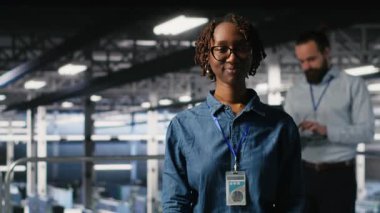 Hataları tespit etmek için ekipman kontrolü yapan iş arkadaşlarının yanında gülümseyen veri merkezi yöneticisinin portresi. Bilgi işlem uzmanlarının yanındaki mutlu kadın arızayı önlemeye ve kapatma süresini en aza indirmeye çalışıyor, kamera B