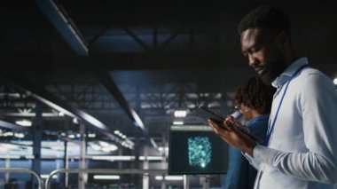 Veri merkezindeki endüstriyel platformda yürüyen mühendis sistem bakımını yapıyor. Güncelleme yapmak, hataları çözmek ve altyapı istikrarını arttırmak için tablet kullanan bilişim uzmanı, kamera A