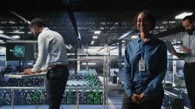 Hataları tespit etmek için ekipman kontrolü yapan iş arkadaşlarının yanında gülümseyen veri merkezi yöneticisinin portresi. Bilgi işlem uzmanlarının yanındaki mutlu kadın arızayı önlemeye ve en aza indirmeye çalışıyor, kamera A