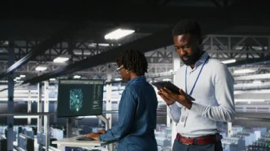 Veri merkezindeki endüstriyel platformda yürüyen mühendis sistem bakımını yapıyor. Güncelleme yapmak, hataları çözmek ve altyapı istikrarını artırmak için tablet kullanan bilişim uzmanı, kamera B