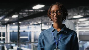Sunucu merkezi mühendisliği ekibinin yanındaki mutlu teknisyen yapay zeka tanılarını inceliyor. Operasyonel güvenilirliği korumak için veri merkezinde çalışan neşeli Afro-Amerikalı kadın, kamera B