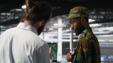 Veri merkezindeki askeri uzmanlar bilgisayardaki İHA görüntülerini inceliyor. Ordu birimleri yüksek teknoloji sunucu odasında savaş alanı keşif operasyonlarını not defteri, kamera B kullanarak yapıyor.