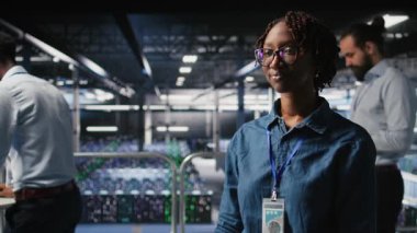 Sunucu merkezi mühendisliği ekibinin yanındaki mutlu teknisyen yapay zeka tanılarını inceliyor. Veri merkezinde çalışan neşeli Afro-Amerikalı kadın operasyonel güvenilirliğini korumak için kamera A