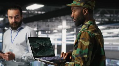 Askeri veri merkezindeki İHA operatörleri dizüstü bilgisayar arayüzü ile otonom uçuş sistemlerini denetliyor. Ekip çalışması bilişim uzmanları not defteri, kamera B kullanarak insansız hava aracı takibi yapıyorlar.