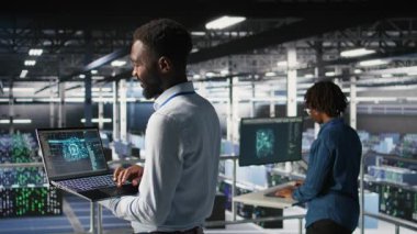 Veri merkezindeki programcı ve meslektaşım bilgisayardaki AI LLM görselleştirmelerini inceliyor. IT ekip çalışanları, istikrarlı altyapı işlemleri sağlamak için nöral ağ performans çıktılarını analiz ederler