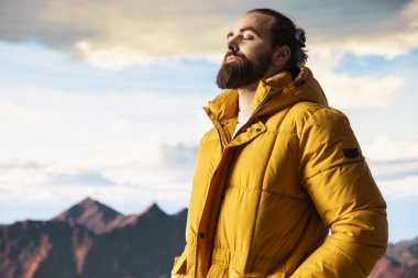 Bir dağ zirvesinde gezgin temiz havayı ve panoramik manzarayı içine çekiyor. Dağcı doğa aşığı engebeli tepelerin, engin gökyüzünün, maceranın ve gezinin çarpıcı manzarasına hayran kalır..