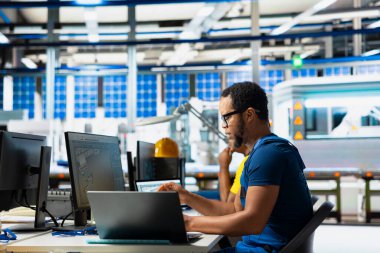 Yenilenebilir enerji tesisindeki bilgisayar kurulumunda güneş enerjisi teknolojisini test eden siyah mühendis, yazılım sorunları ve performans ölçümlerine odaklanıyor. Çevre dostu sürdürülebilir operasyonları desteklerName.