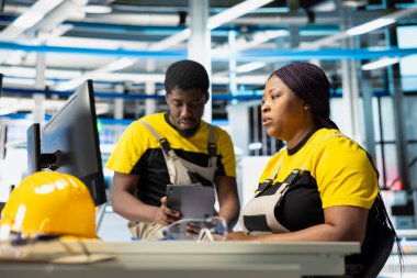 Robot silahlarının performansını değerlendiren fotovoltaik fabrikası yöneticileri güneş panellerini montaj hattına yerleştirip sürdürülebilir enerji üretiyorlar. Tüm siyah takımlar üretim sürecine bakıyor..