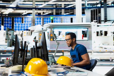 Erkek mühendis güneş paneli fabrika üretim hatlarını denetlemek için bilgisayar kurulumunu, robotik kollarla sorunsuz üretim hattını yönetmek için fotovoltaik sistemi kullanıyor. Yenilenebilir enerji.