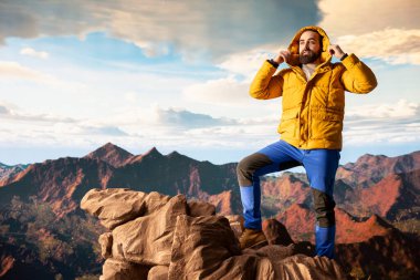 Doğa aşığı nefes kesen bir dağ sırasının kenarında duruyor, yükselen zirvelerin ve uçsuz bucaksız gökyüzünün manzaralı arka planına bakıyor. Genç adam macera ve açık hava keşiflerini seviyor..