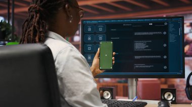 Kadın yeşil ekranlı telefon kullanıyor, AI LLM sohbet robotuyla ekranın önünde video görüşmesi yapıyor. Kişi, telekonferans sırasında akıllı telefon, kamera B 'de büyük dil modeli programı kullanır.