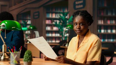 Geleneksel bir kütüphane ortamında siyahi öğrenci, eğitim hedeflerine ve kampüs içinde ders çalışma saatlerine odaklanıyor. Üniversiteli kız okuyor ve araştırma yapıyor. Kamera B.