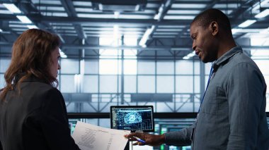 Bilgi işlem uzmanlarından oluşan bir ekip veri merkezinin kontrol evraklarını inceliyor, tabletteki yapay zeka teknolojisini kullanıyor. Sunucu çiftliğinde iş birliği yapan meslektaşlar, yapay zeka, kamera B, belge okuyorlar.