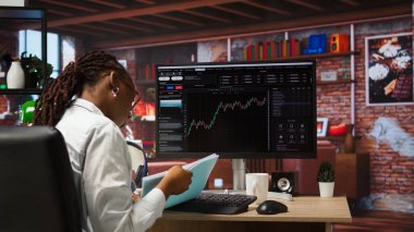 Borsa simsarı hisse senedi alıp satmak için bilgisayar kullanıyor. Kârın nasıl maksimuma çıkarılacağını öğrenmek için doküman dosyalarına göz atıyor. Bilgisayar monitöründeki borsa grafiklerine bakan yatırımcı, kamera A