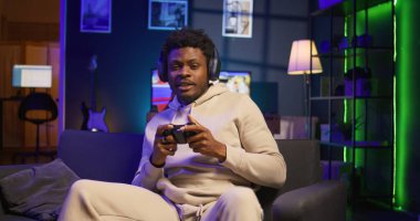 Evdeki kanepede oturan genç adam oyun konsolunda video oyunları oynayarak rahatlıyor, neon ışıklı apartman dairesinde internetteki çoklu oyuncu ve spor turnuvasında rekabet ederek gevşiyor. Kamera B.