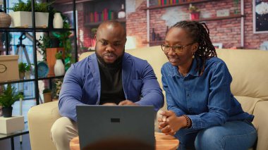 Siyahi genç bir çift evlerinde video bağlantısı kuruyor, kanepede oturuyor ve arkadaşlarıyla konuşuyor. Kadın ve erkek video konferansında el sallıyor, yaşam tarzı. Kamera A.