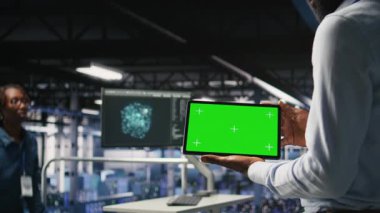 Nöro ağ çıktılarını analiz etmek için krom anahtar aygıt kullanan bilişim uzmanlarını kapatın. Veri merkezi yönetimi, bulanık arkaplanda yapay zeka görsellemesini inceleyen meslektaşının yanında yeşil ekran tableti kullanır