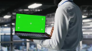 Veri merkezi endüstriyel platformundaki mühendislere yaklaşıp yeşil ekran laptopundaki performans çıktılarını analiz edin. Sunucu odası IT uzmanı sunucu sondaj ayarlarını model defter, kamera B kullanarak inceliyor