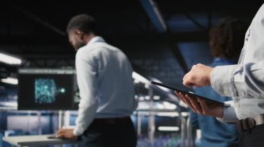 Sunucu odası çalışanının AI LLM görselleştirmesini inceleyen meslektaşının yanındaki tablet üzerindeki kodu kontrol etmesini kapat. Veri merkezi bilişim uzmanı yapay zeka sistemlerini, kamera A 'yı izlemek için aygıt kullanıyor