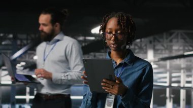 Veri Merkezi çalışanı mikrofonla konuşurken aşağıdaki yapay zeka platformlarının bakımını denetliyor. IT uzmanı, makine öğrenme sistemi görevlerini takım ile koordine etmek için tablet kullanır