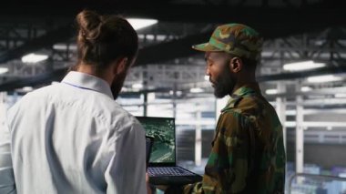 Veri merkezindeki ordu operatörleri İHA kontrol yazılımını çalıştırmak için dizüstü bilgisayar kullanarak görev haritasına bakıyorlar. Askeri uzmanlar otonom hava araçlarının stratejik konuşlandırılmasını yapıyorlar, kamera B
