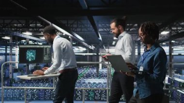 Veri merkezindeki mutlu kadın laptopta bakım görevleri yapıyor ve en iyi performansı sağlıyor. Mühendislik ekibi tanıları inceliyor ve sunucu odasına yama uyguluyor, istikrarı artırıyor, kamera A