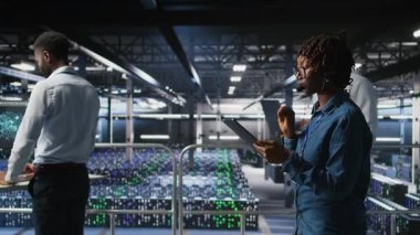 Sunucu odası yönetimi, altyapı teknik desteği sağlamak için tablet ve kulaklık mikrofonu kullanıyor. Veri merkezi bilişim uzmanı uzak ekipler, kamera A ile koordine ederken arka uç sorunlarını çözer