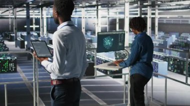 Veri merkezi programcısı kod satırlarını kontrol ediyor ve iş arkadaşı AI LLM görselleştirmelerini inceliyor. IT uzmanları, tablet kullanarak istikrarlı altyapı işlemleri sağlamak için nöral ağ çıktılarını analiz ederler