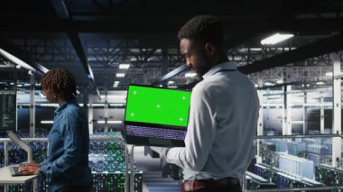 Veri merkezindeki teknisyenler yeşil ekran laptopundaki performans çıktılarını analiz ediyorlar. Sunucu merkezi mühendislik ekibi sunucu sondaj ayarlarını model defter, kamera A kullanarak inceliyor.