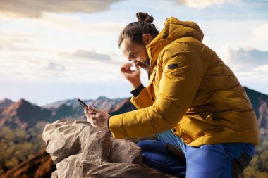 Genç gezginin dikkatini dağın tepesindeki telefonu dağıtıyor, teknoloji bağımlılığıyla uğraşıyor ve her zaman internete bağlı. Kâşif manzaranın tadını çıkarıyor.