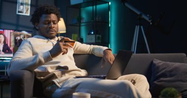 Gülümseyen Afro-Amerikalı bir adam para transferini onaylamak için kart numaralarına giriyor ve bilgisayarından online alışveriş için ödeme yapıyor. Sipariş verdikten sonra mutlu insan kendini iyi hissediyor. Kamera B.