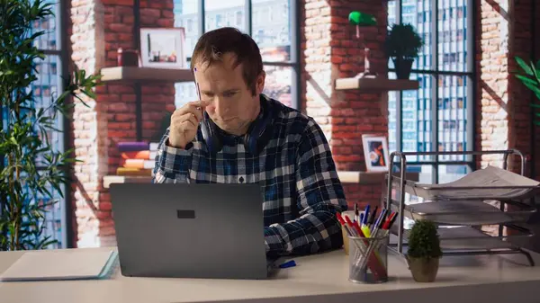 Ofisteki stresli adam dizüstü bilgisayarında çok fazla e-posta cevapladıktan sonra kafasını kalemle kaşıyordu. Yorgun tele-işçi, çok fazla proje görevi ve kamera A 'dan dolayı kendini yorgun hissediyor.