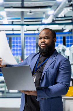 Güneş paneli makinelerini kontrol eden ve bir kontrol listesini inceleyen fabrika çalışanı, yenilenebilir enerji üretimi ve montaj hattında hayati bir rol oynuyor. Verimli güneş teknolojisi altyapısı.