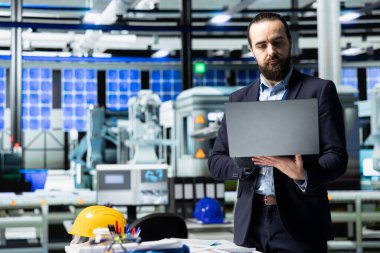 Sanayi işyerindeki güneş enerjisi sistemlerini denetleyen idari danışman, sürdürülebilir enerji gelişimi için stratejik planlamayı vurguluyor. Temiz enerji üretim hattında yenilik.