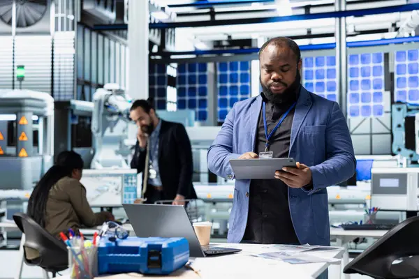 Afrikalı Amerikalı denetçi güneş paneli makinelerini kontrol ediyor ve yenilenebilir enerji üretimi ve üretim hattında hayati bir rol oynayan bir kontrol listesini gözden geçiriyor. Verimli güneş teknolojisi altyapısı.