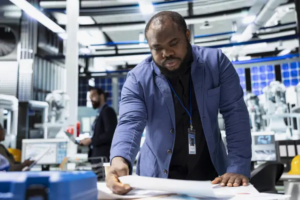 Siyah erkek sürdürülebilirlik danışmanı güneş paneli sistemlerini ve modern bir fabrikadaki üretim hattını değerlendirerek temiz enerji ve endüstriyel verimliliğe yönelik operasyonlara rehberlik ediyor..