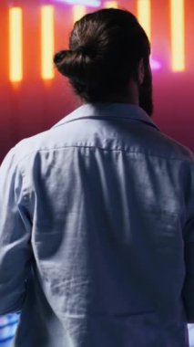 Dikey video gündelik genç adam parlak neon ışıklara canlı renklerle bakıyor, fütürist siber punk atmosferinin tadını çıkarıyor. Bir gece sahnesinde kentsel tarz ve yaratıcılık gösteriliyor