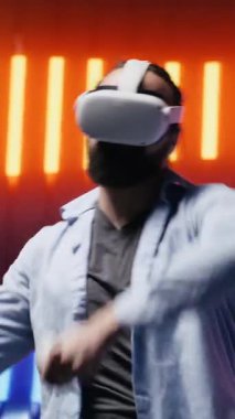 Dikey Video Havalı modern adam sanal gerçeklik gözlükleriyle sanatsal titreşimler sergiliyor, eğlence için siber punk atmosferinde renkli neon ışıklarla çevrili. Gece hayatı minimalizmi. Kamera.
