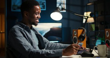 Afrikalı Amerikalı bir adam internet sayfasından kredi kartı bilgilerini giriyor ve online kıyafet dükkanına ödeme yapmaya hazırlanıyor. Dizüstü bilgisayardaki alışveriş çılgınlığı sırasında genç adam dijital para transferini kabul ediyor. Kamera A.