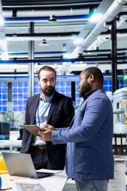 Üretim denetimi sırasında güneş paneli sistemlerini analiz eden bir grup endüstri uzmanı ve mühendis mühendislik mühendisliği doğruluğu, kalite kontrolü ve fabrika faaliyetlerinin verimliliğini güvence altına alıyor.